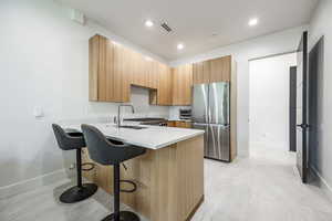 Kitchen with freestanding refrigerator, a peninsula, a kitchen bar, light countertops, and baseboards