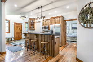Kitchen with appliances with stainless steel finishes, light wood-style flooring, dark countertops, a breakfast bar, and brown cabinetry