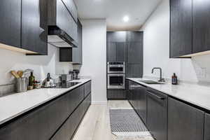 Kitchen featuring a sink, black electric cooktop, light countertops, light wood-style floors, and double oven