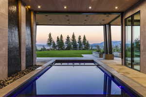 Pool at dusk with a mountain view, a yard, an outdoor pool, and a patio