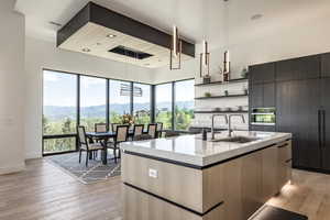 Kitchen featuring a sink, modern cabinets, open shelves, light wood finished floors, and a center island with sink