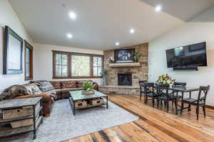Living room featuring hardwood / wood-style floors, vaulted ceiling, a stone fireplace, and recessed lighting