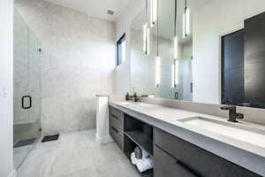 Full bath featuring double vanity, a stall shower, and marble look tile flooring