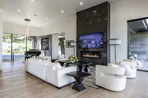 Living room with a tiled fireplace, recessed lighting, light wood finished floors, and a high ceiling