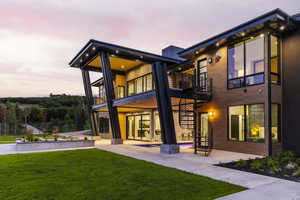 Back of property at dusk featuring a balcony, a yard, a patio area, and stairs