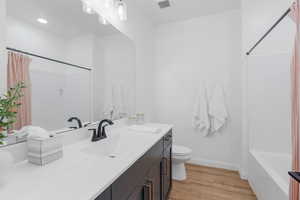 Full bathroom with toilet, shower / bath combination with curtain, hardwood / wood-style floors, and vanity