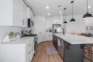 Kitchen with lofted ceiling, light hardwood / wood-style flooring, a kitchen island with sink, stainless steel appliances, and a kitchen bar