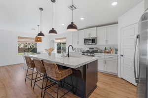 Kitchen with decorative light fixtures, an island with sink, a breakfast bar area, appliances with stainless steel finishes, and light hardwood / wood-style flooring