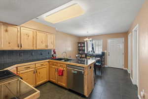 Kitchen featuring a textured ceiling, kitchen peninsula, stainless steel dishwasher, dark tile patterned flooring, and sink