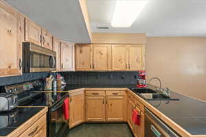 Kitchen with stainless steel appliances, sink, dark tile patterned flooring, backsplash, and tile counters