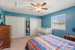 Carpeted bedroom featuring multiple closets and ceiling fan