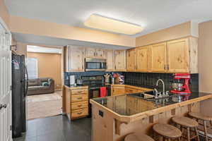 Kitchen featuring black refrigerator, kitchen peninsula, tasteful backsplash, and dark carpet