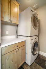 Laundry area featuring cabinets, dark tile patterned floors, and stacked washer and clothes dryer