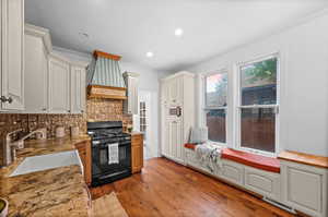 Kitchen featuring sink, backsplash, custom exhaust hood, black gas range, and wood-type flooring