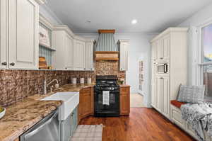 Kitchen featuring stainless steel dishwasher, black gas range, light stone counters, backsplash, and dark wood-type flooring