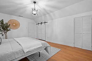 Bedroom with lofted ceiling, an inviting chandelier, wood-type flooring, and a barn door