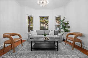 Living area featuring an inviting chandelier, wood-type flooring, and ornamental molding