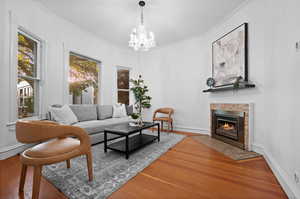 Living room with a fireplace, crown molding, hardwood / wood-style floors, and an inviting chandelier