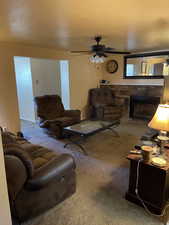 Carpeted living room featuring a fireplace, a textured ceiling, and ceiling fan