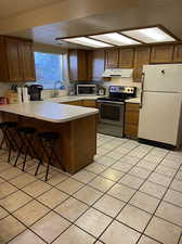 Kitchen featuring a kitchen bar, appliances with stainless steel finishes, sink, kitchen peninsula, and light tile patterned floors