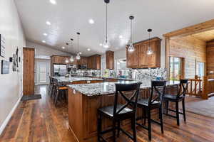 Kitchen featuring lofted ceiling, a breakfast bar, dark hardwood / wood-style floors, stainless steel appliances, and pendant lighting