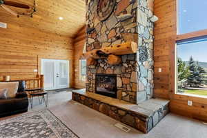 Living room featuring carpet flooring, wood walls, ceiling fan, a fireplace, and high vaulted ceiling