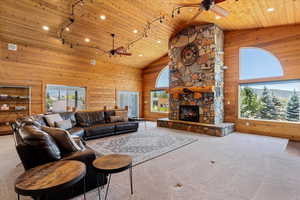 Carpeted living room with a stone fireplace, wooden ceiling, a wealth of natural light, and ceiling fan