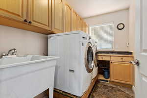 Laundry room with washing machine and dryer, dark tile patterned flooring, and cabinets