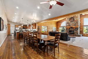 Dining space featuring a stone fireplace, dark hardwood / wood-style floors, vaulted ceiling, and ceiling fan with notable chandelier