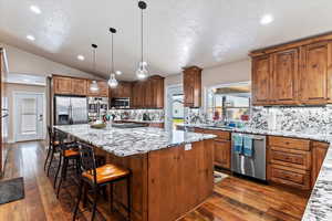 Kitchen featuring lofted ceiling, a center island, backsplash, dark wood-type flooring, and stainless steel appliances