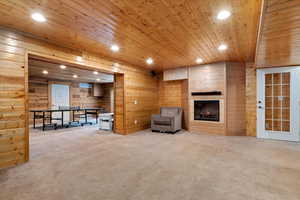 Unfurnished living room featuring a large fireplace, light colored carpet, wood walls, and wood ceiling