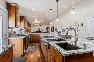 Kitchen featuring sink, light stone counters, hanging light fixtures, a kitchen island, and dark hardwood / wood-style floors