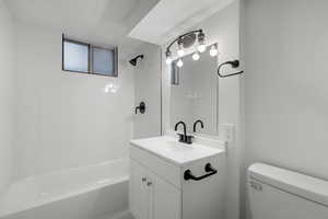 Full bathroom with vanity, tiled shower / bath combo, and toilet