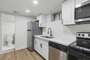 Kitchen featuring stainless steel appliances, sink, decorative backsplash, light wood-type flooring, and white cabinetry