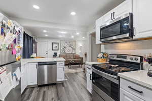 Kitchen with white cabinets, backsplash, stainless steel appliances, light stone countertops, and wood-type flooring