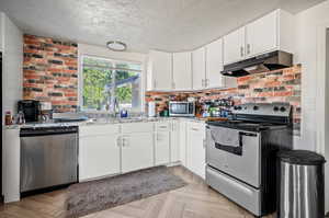 Kitchen with appliances with stainless steel finishes, light parquet flooring, light stone countertops, and sink