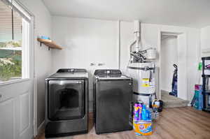 Washroom featuring washer and clothes dryer, secured water heater, and light wood-type flooring