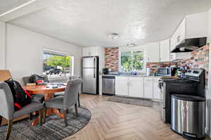 Kitchen with light parquet floors, stainless steel appliances, decorative backsplash, white cabinets, and a textured ceiling