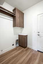 Clothes washing area featuring light wood-type flooring, hookup for an electric dryer, cabinets, and a textured ceiling