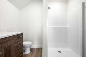 Bathroom with vaulted ceiling, toilet, a shower, wood-type flooring, and vanity
