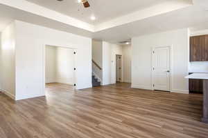 Unfurnished living room featuring light hardwood / wood-style flooring, ceiling fan, and a raised ceiling
