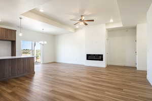 Unfurnished living room with ceiling fan with notable chandelier, a textured ceiling, a tray ceiling, and light hardwood / wood-style floors