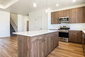 Kitchen featuring light hardwood / wood-style flooring, decorative light fixtures, appliances with stainless steel finishes, and a kitchen island