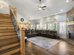 Living room with a high ceiling, ceiling fan, wood-type flooring, and a stone fireplace