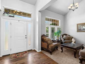 Entryway featuring a notable chandelier, a wealth of natural light, high vaulted ceiling, and dark wood-type flooring