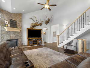 Living room with a high ceiling, wood-type flooring, a stone fireplace, and ceiling fan