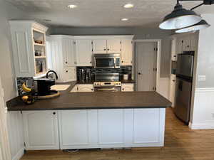 Kitchen featuring appliances with stainless steel finishes, white cabinets, sink, kitchen peninsula, and decorative backsplash