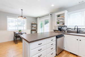 Kitchen with light hardwood / wood-style floors, dishwasher, tasteful backsplash, and decorative light fixtures