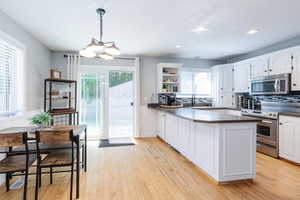 Kitchen featuring hanging light fixtures, a healthy amount of sunlight, white cabinets, decorative backsplash, and appliances with stainless steel finishes