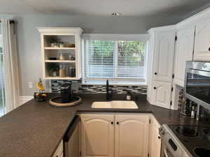 Kitchen featuring stainless steel appliances, sink, backsplash, a textured ceiling, and white cabinetry